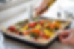 pouring oil over a traybake of vegetables
